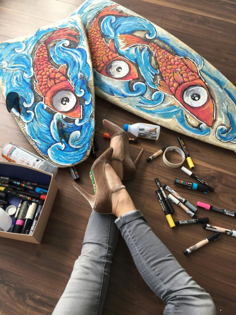 Colorful surfboards painted with fish designs surrounded by art supplies and stylish shoes.