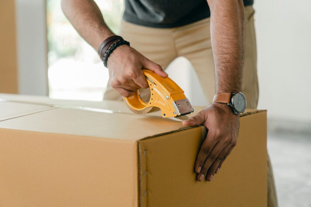 pexels photo 4246120 4246120 Crop faceless young male with wristwatch using adhesive tape while preparing cardboard box for transportation