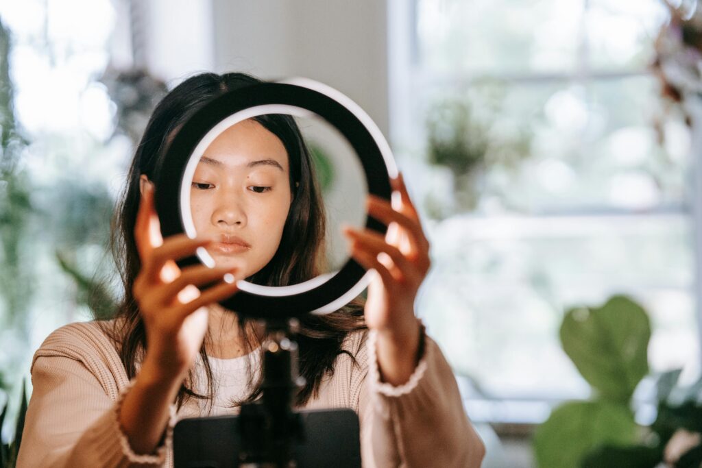 An Asian woman setting up a ring light indoors, focusing on her face and hands.